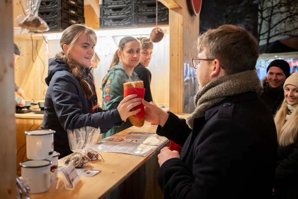 Man sieht eine Frau, wie sie einem Mann einen Hotdog über die Theke reicht. 